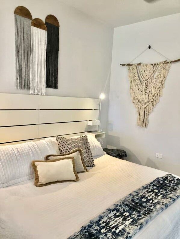 A bedroom with a large bed, white headboard, and decorative macramé wall hanging. - Studio Mare Ground Steps to pool @ Palmas del Mar (Humacao)