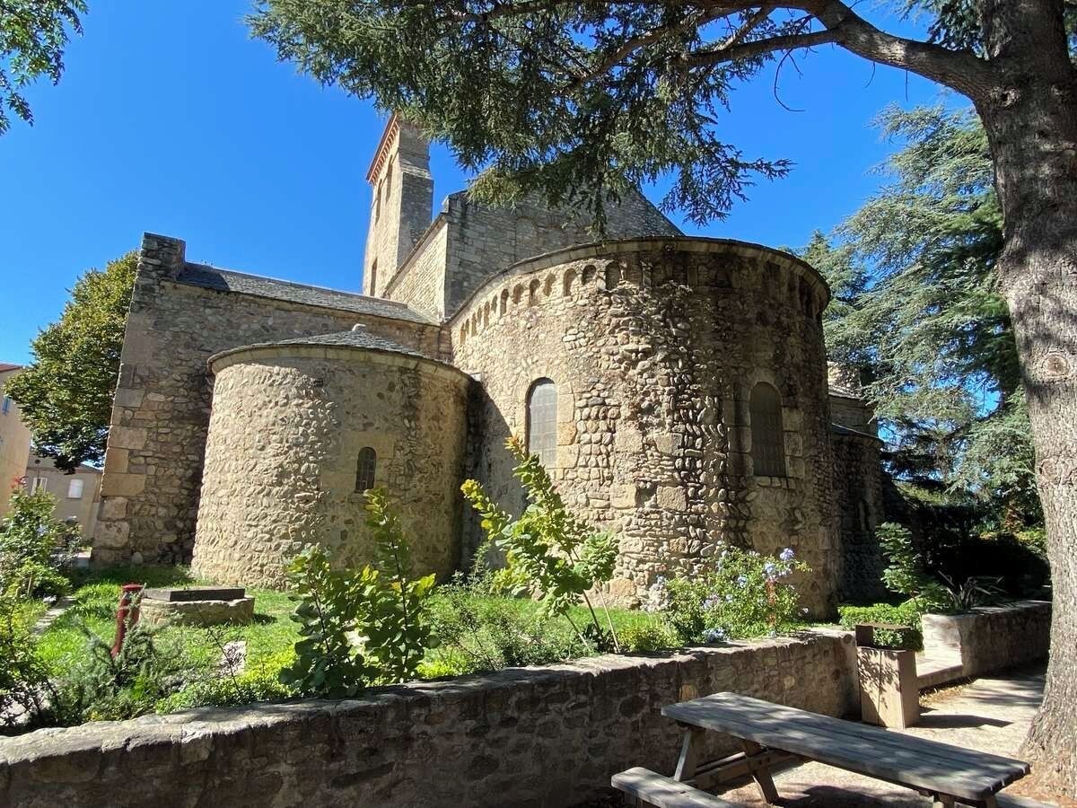 A stone building with a tower and arched windows, surrounded by greenery and a picnic table.