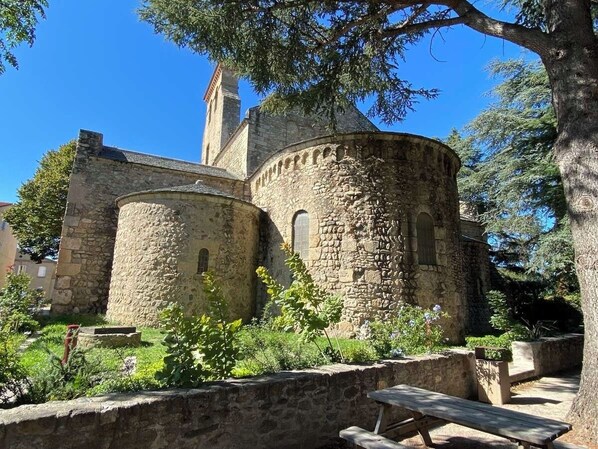 A stone building with a tower and arched windows, surrounded by greenery and a picnic table.