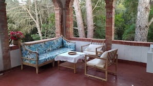 Une terrasse couverte avec un canapé bleu à motifs, une petite table et deux chaises.
