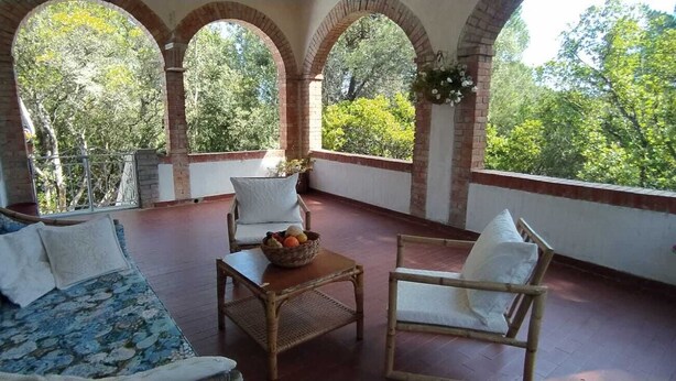 Une terrasse couverte avec un canapé, des fauteuils et une table sur laquelle sont disposés des fruits.