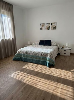 A bedroom with a bed, a nightstand, a lamp, and a window with curtains. - Southern Cross – Nature and Sea in Sicily, ideal for families and groups (Sicilia)