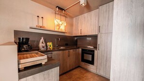 A compact kitchen with wooden cabinets, a built-in oven, and a coffee maker. - 3-bedroom apartment Frauenschuh 2-10 pers (110m2), terrace & view of the slopes (Berwang)