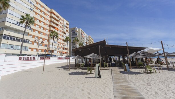 A beachside hotel with outdoor seating, palm trees, and a view of the sea.