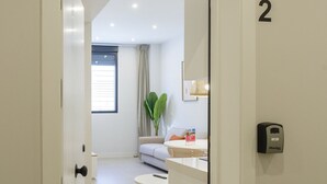 En moderne, veloplyst gang, der fører til et opholdsområde med sofa, spisebord og et planter.