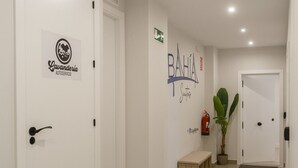 A clean, modern hallway with white walls, a fire extinguisher, and a potted plant. - BAHIA Suite -apart. adaptado- (Cádiz)