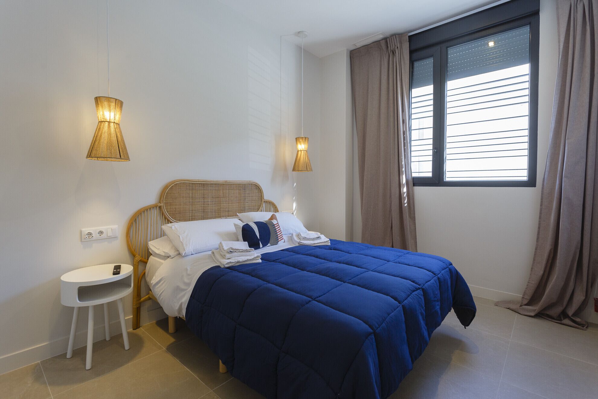 Un dormitorio con cama, dos lámparas de noche, una mesita blanca y una ventana con cortinas.