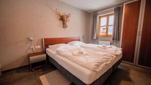 Een slaapkamer met een houten hoofdbord, een groot bed met witte lakens, een nachtkastje, een op de muur bevestigd decoratie van een stierenhoofd, een raam met gordijnen en een kledingkast.