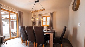 Een eetgedeelte met een houten tafel, zes stoelen, een kroonluchter en uitzicht door grote ramen.