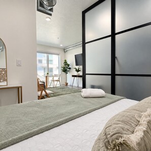 A modern hotel room with a large bed, a desk, a chair, a TV, and a sliding door. - Modern Downtown Apt| King Bed+Pool+Prime Location (Salt Lake City)