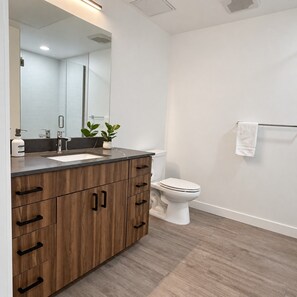 A modern bathroom with a wooden vanity, a white toilet, and a towel rack. - Modern Downtown Apt| King Bed+Pool+Prime Location (Salt Lake City)