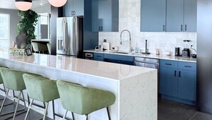 A modern kitchen with a central island, bar stools, blue cabinets, and pendant lighting.