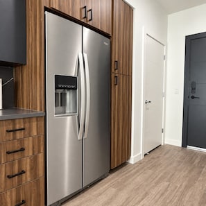 A modern kitchen with a stainless steel refrigerator, wooden cabinetry, and a white door. - Modern Downtown Apt| King Bed+Pool+Prime Location (Salt Lake City)