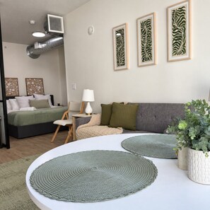 A modern bedroom with a bed, a sofa, a small table, and a potted plant. - Modern Downtown Apt| King Bed+Pool+Prime Location (Salt Lake City)