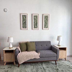A neutral-toned living room with a grey sofa, two green cushions, a knitted throw, and three framed abstract leaf patterns on the wall. - Modern Downtown Apt| King Bed+Pool+Prime Location (Salt Lake City)