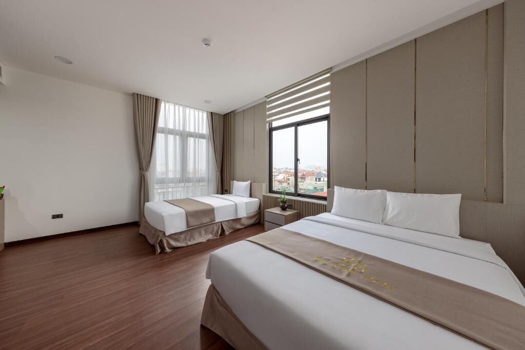 Une chambre d’hôtel avec un grand lit, un lit plus petit, une table de chevet, une fenêtre avec des stores et une vue sur la ville.