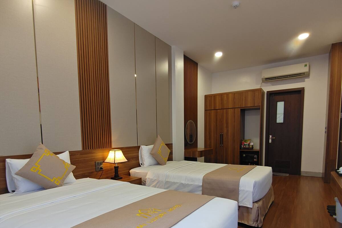 A hotel room with two beds, wooden paneling on the walls, a ceiling light, an air conditioning unit, and a door.
