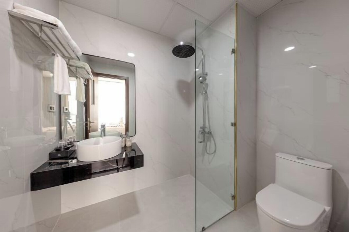 Un baño moderno con ducha de vidrio, inodoro blanco y tocador con lavabo y espejo.