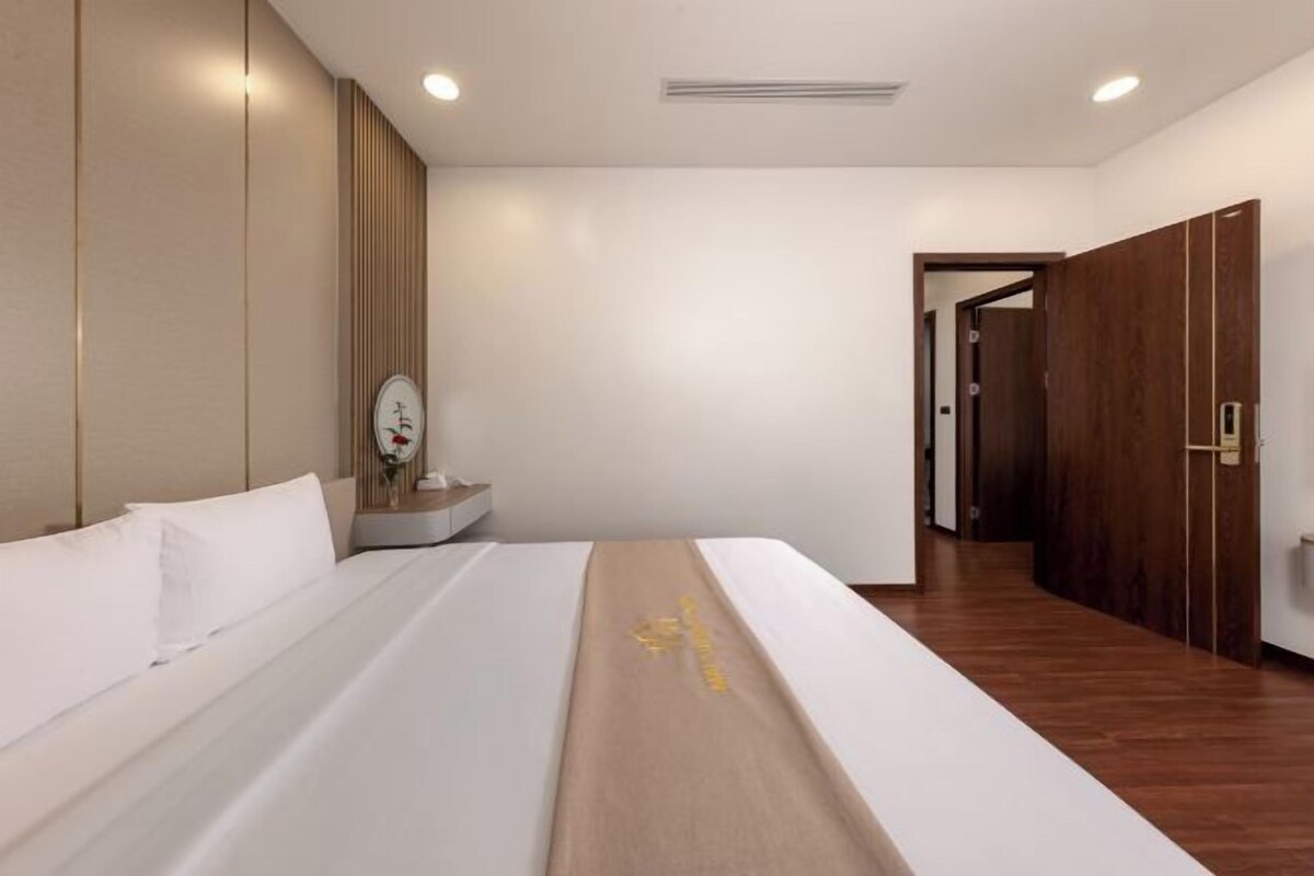 Una habitación de hotel con una cama grande, una mesita de noche de madera, un atril y un armario.