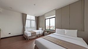 A hotel room with a large bed, two smaller beds, a nightstand, a window with blinds, and a view of the city. - MAI Luxury Hotel Ninh Binh (Ninh Binh)