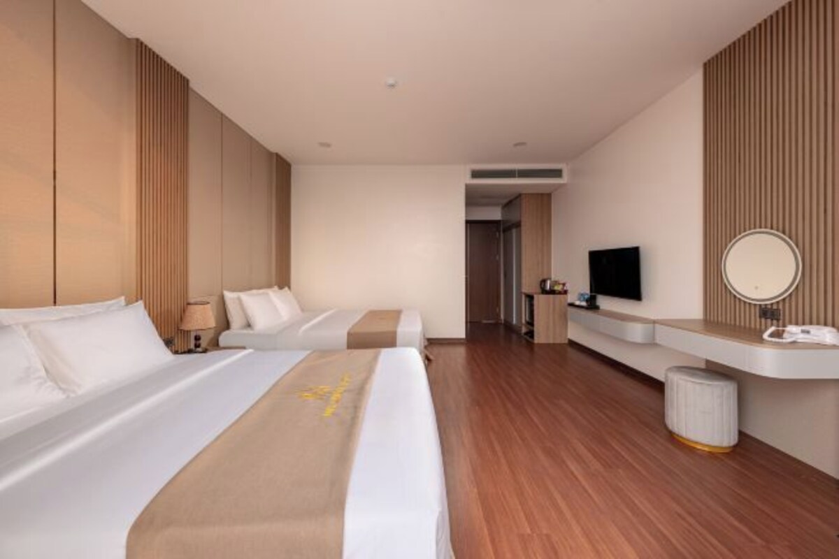 Una habitación de hotel moderna con dos camas, un televisor de pantalla plana, un tocador con espejo y una pequeña zona de estar.