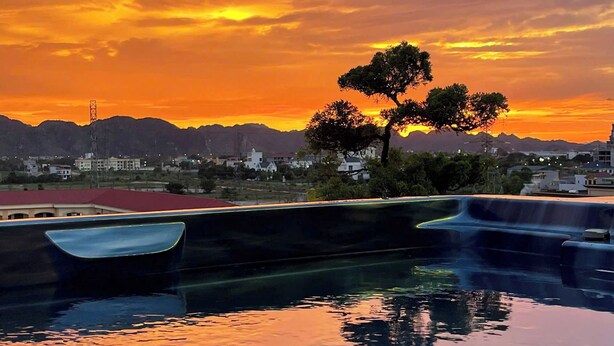 A swimming pool with a sunset view, a tree, and distant buildings. - MAI Luxury Hotel Ninh Binh (Ninh Binh)