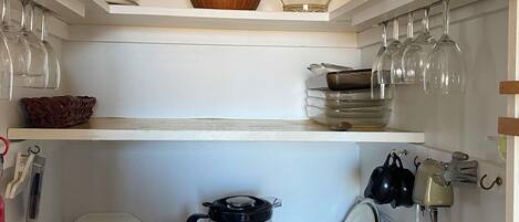 Una cocina con estantes blancos que sostienen diferentes utensilios de cocina, un tostador y una licuadora sobre la encimera.