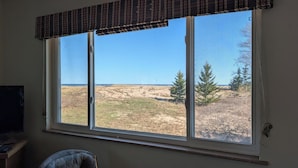 A room with a large window overlooking a grassy field and trees. - Agate Beach House - waterfront in Grand Marais (Grand Marais)