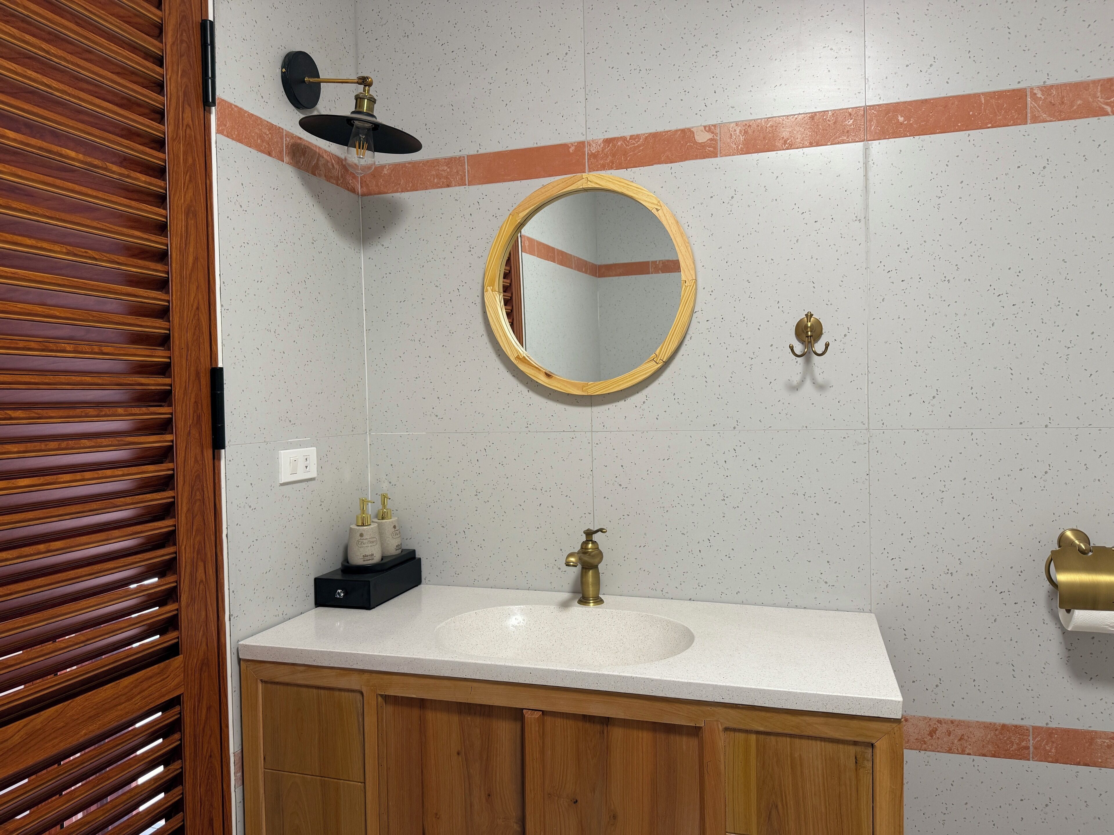 A bathroom with a wooden vanity, a round mirror, a shower with a black handle, and a towel rack.