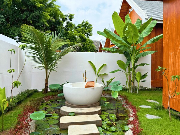 A serene garden with a large white bathtub, lush greenery, and stepping stones leading to a pond with lily pads. - The Jam Boutique Hotel (Luang Prabang)