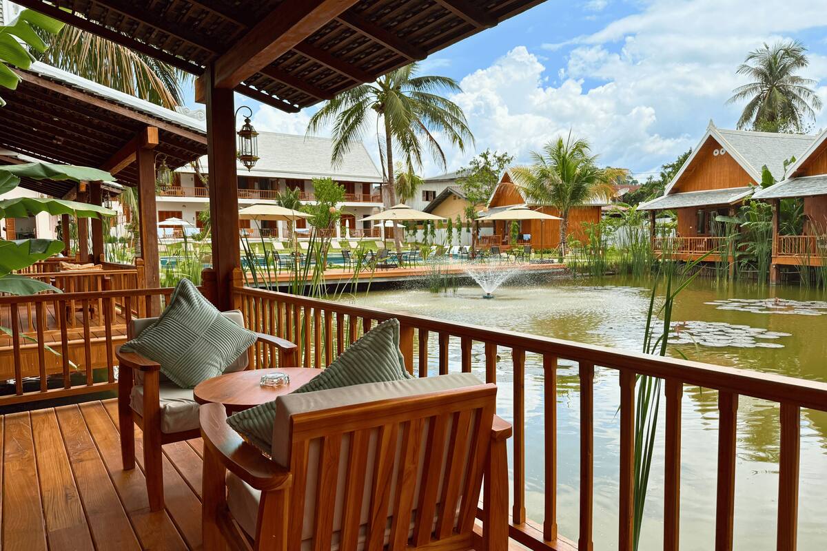 A wooden deck with a view of a pool and palm trees.