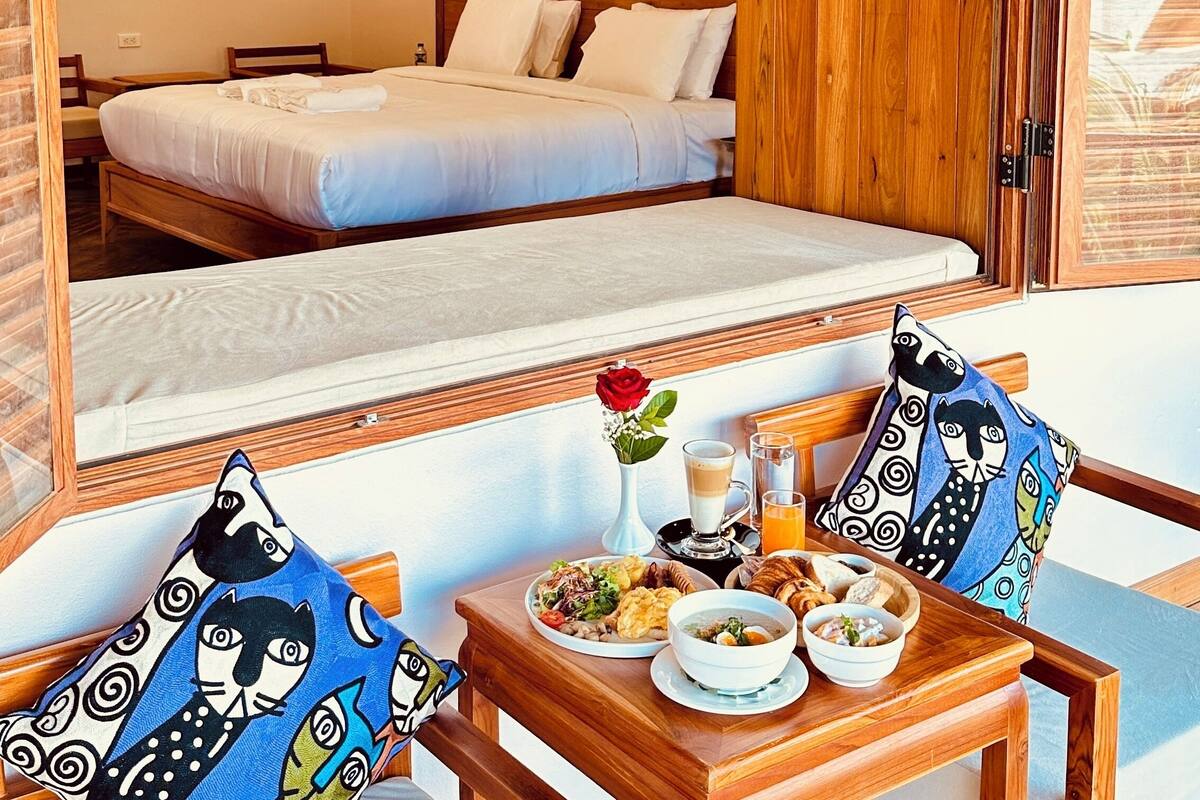 A hotel room with a bed, a dining table with breakfast, and a view of the sea.