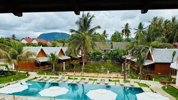 A resort with a swimming pool, lounge chairs, and palm trees.