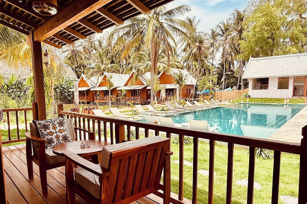 A wooden deck with a pool, lounge chairs, and a view of overwater bungalows.