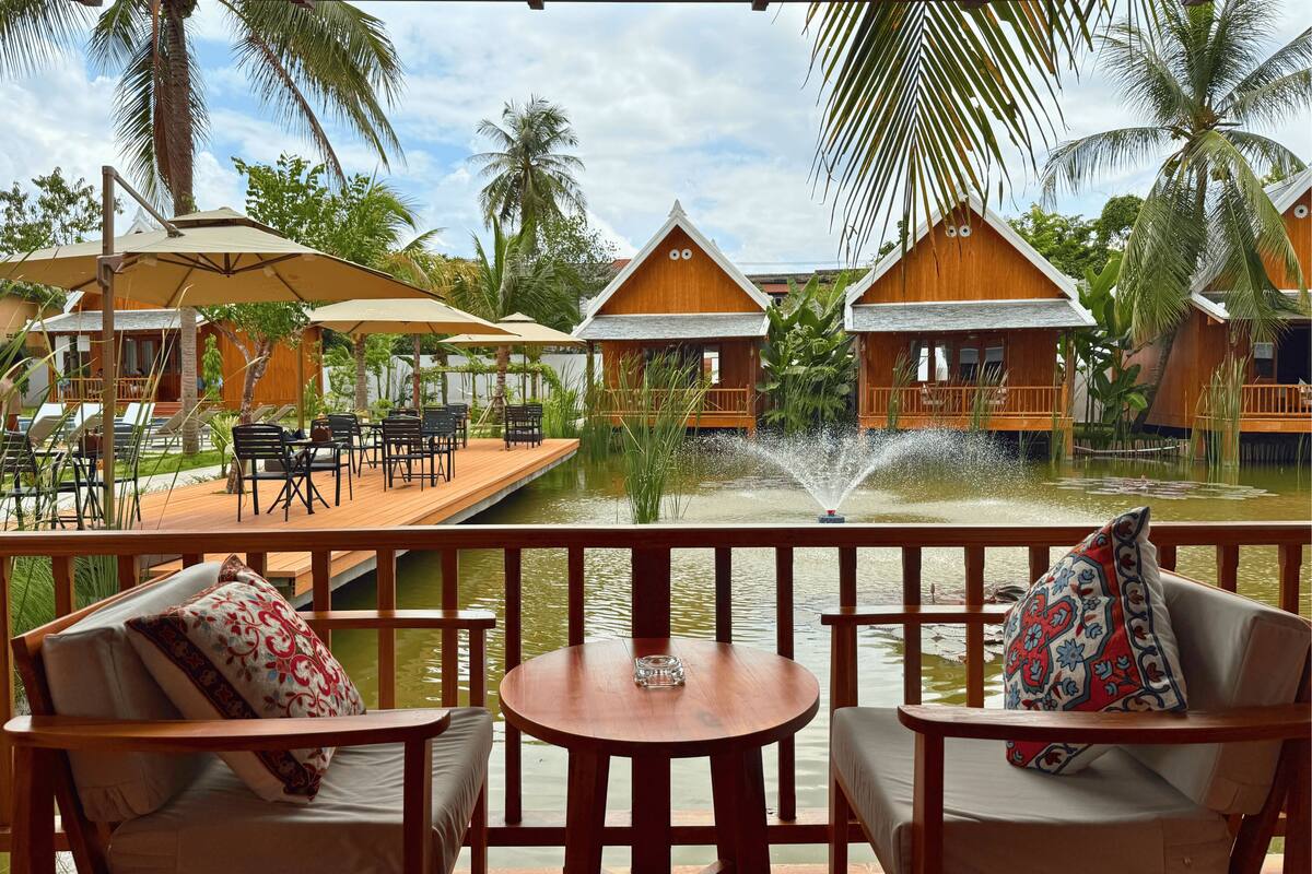 A wooden deck with outdoor seating, a water feature, and overwater bungalows.