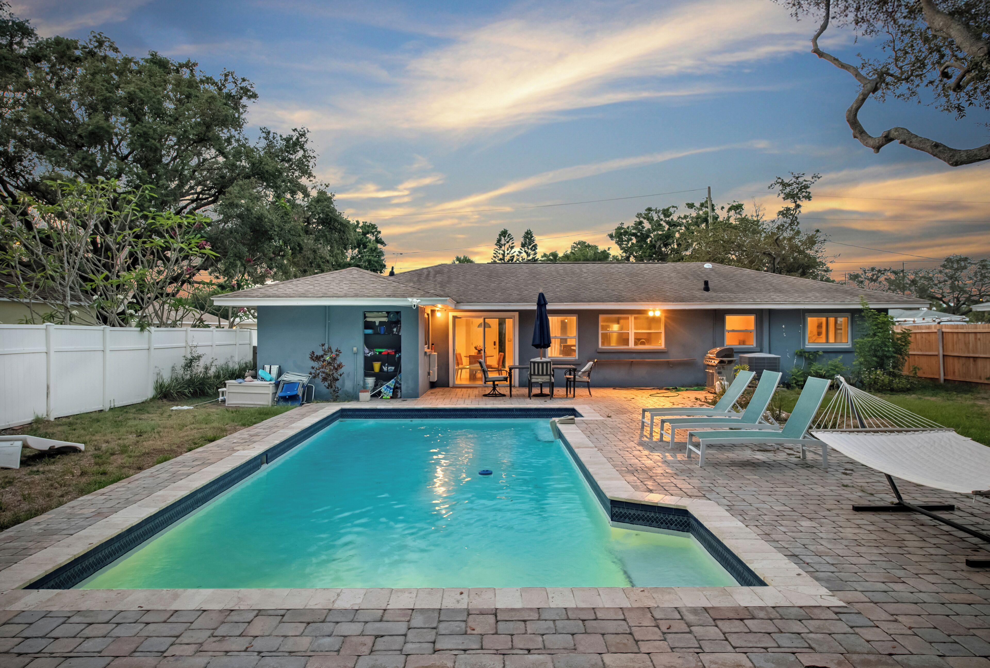 A backyard with a swimming pool, lounge chairs, and a barbecue area.
