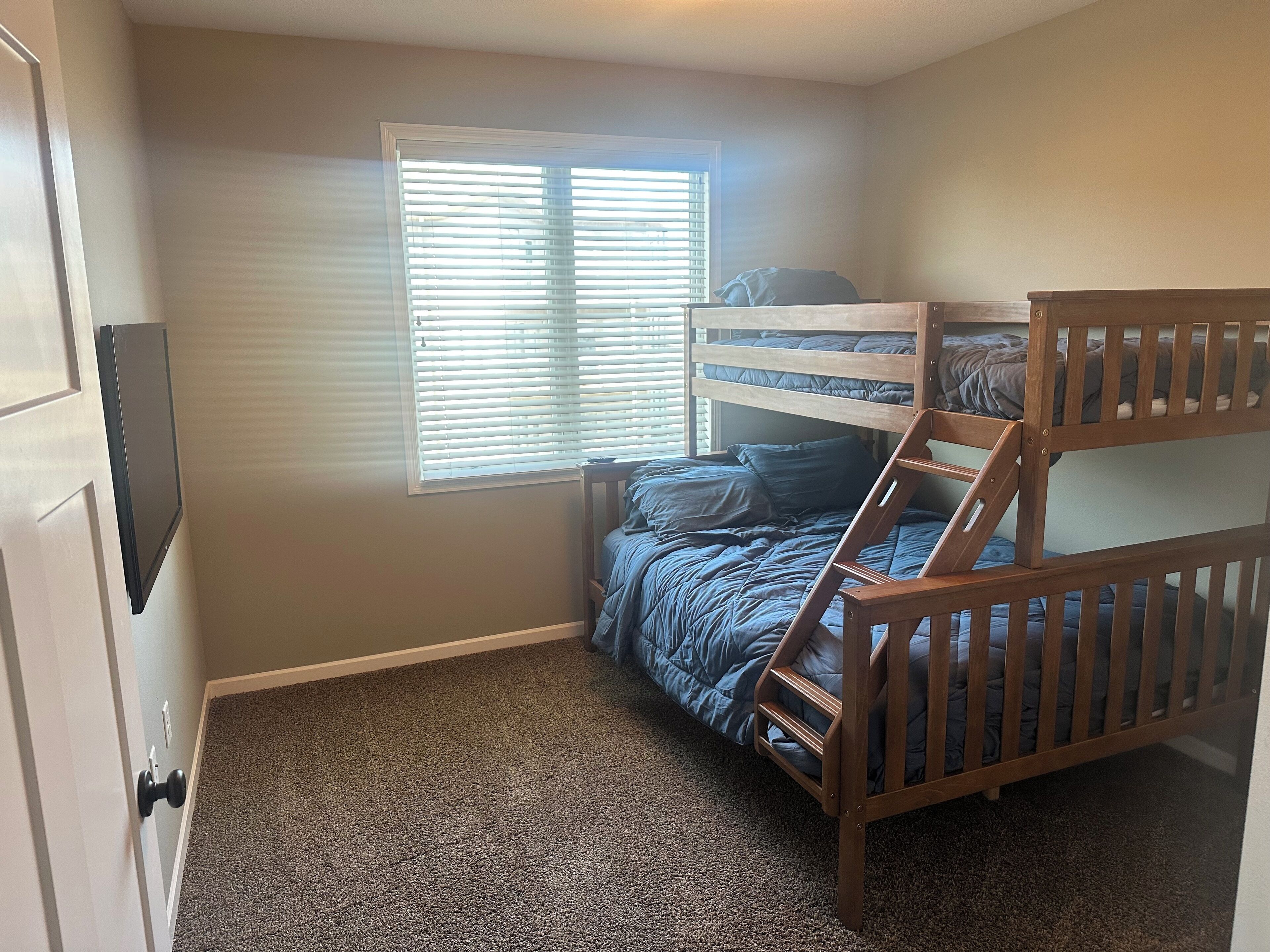 A bedroom with a bunk bed, a window with blinds, and a carpeted floor.