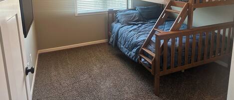 A bedroom with a bunk bed, a window with blinds, and a carpeted floor.