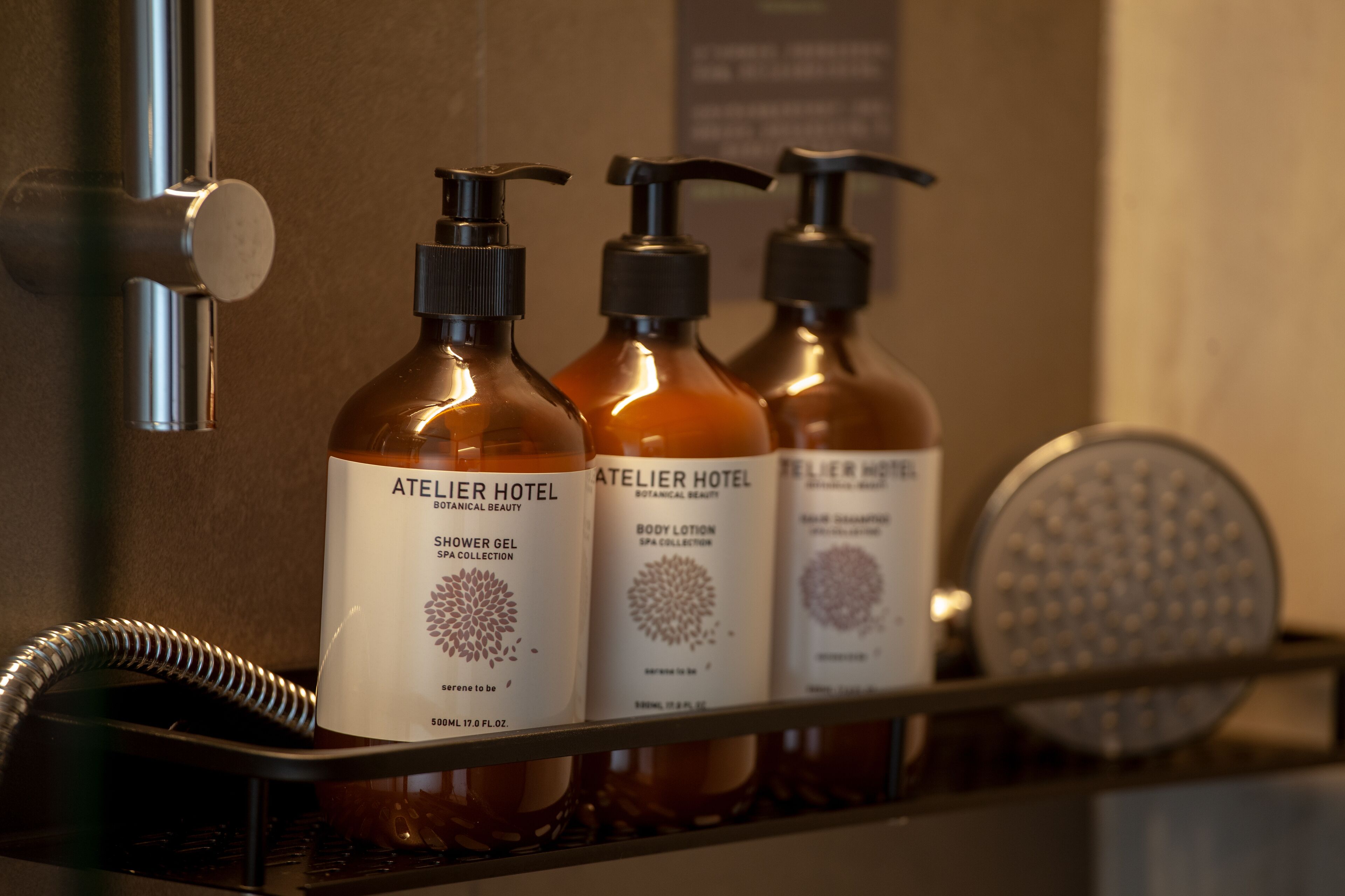 Three shower bottles labeled 'Atelier Hotel' on a shelf.