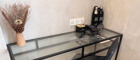 A modern glass desk with a black chair, a vase with dried plants, and a hair care product display.