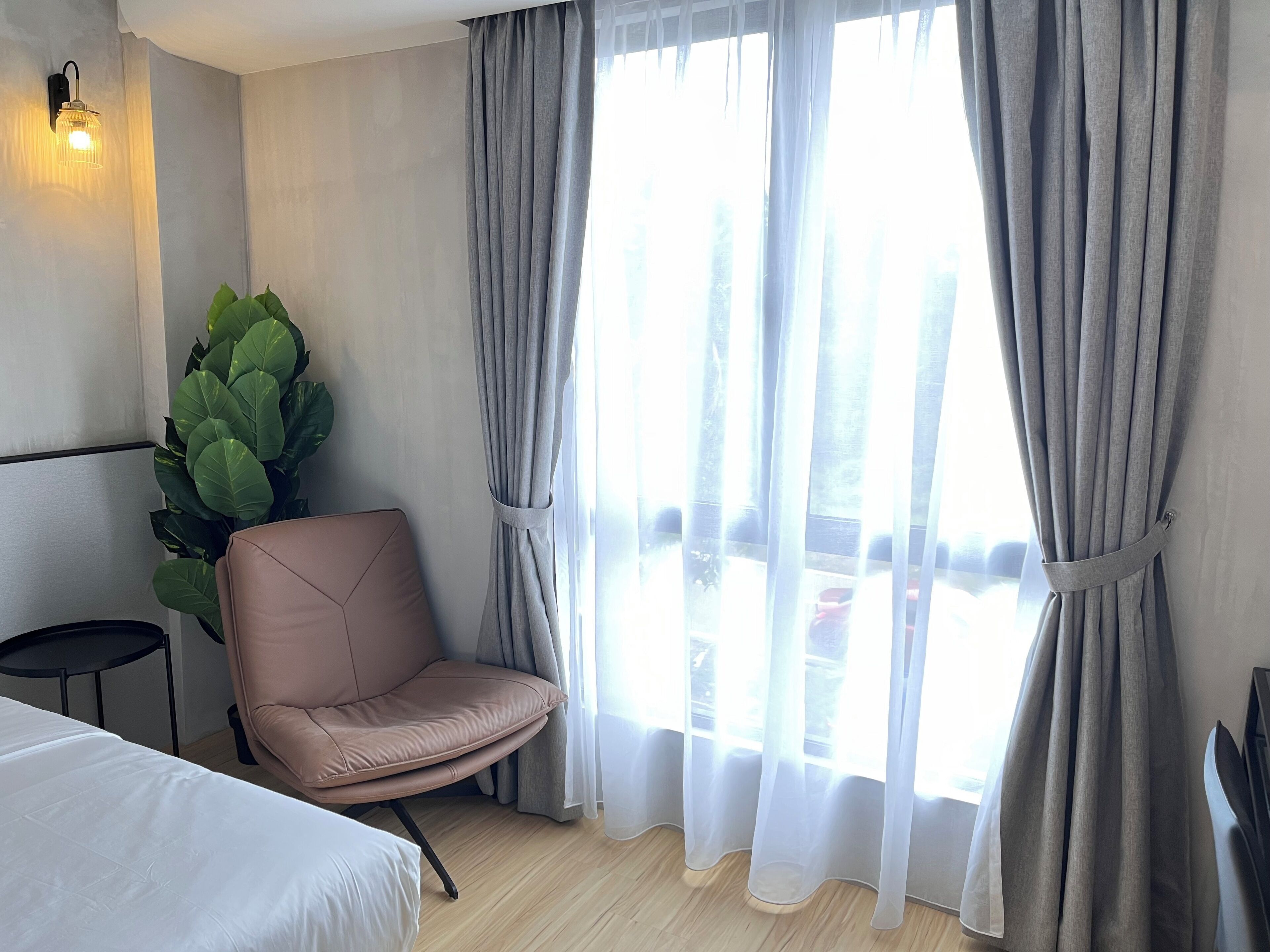 Habitación de hotel con cama, una silla, una planta en maceta y una ventana con cortinas.