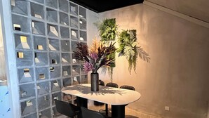 Un comedor moderno con una mesa redonda, dos sillas negras, un jarrón con flores y una pared decorativa con un diseño geométrico.