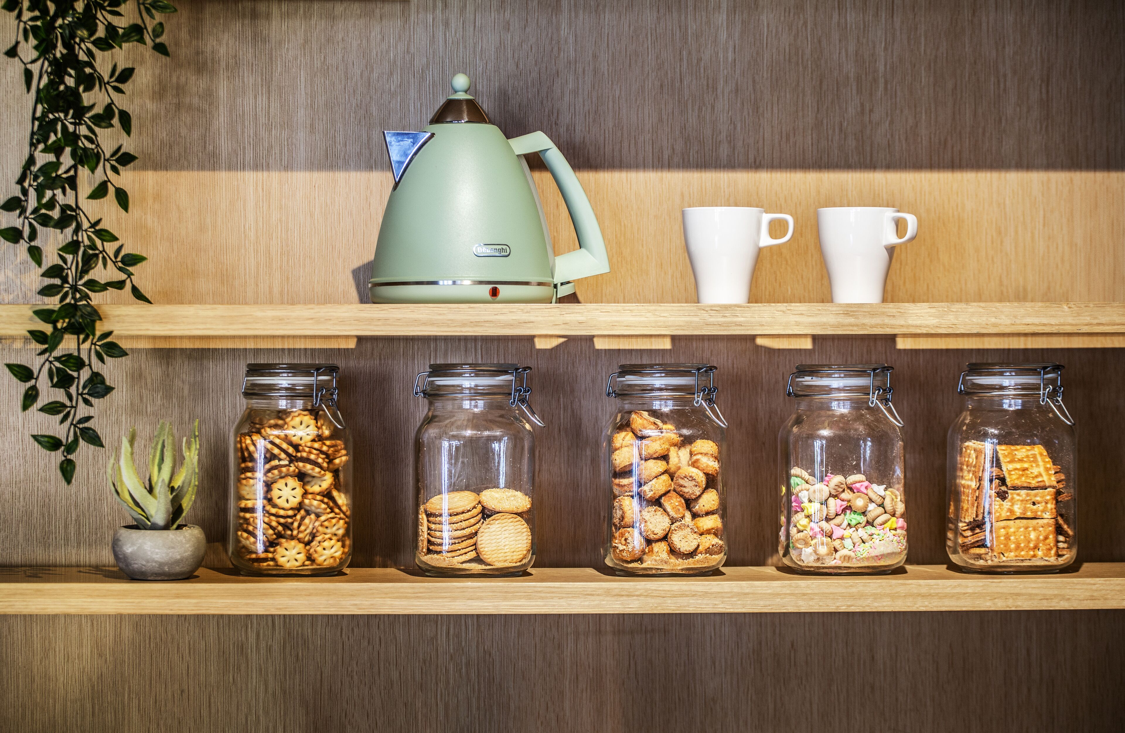 Una estantería con botes de galletas, una tetera y dos tazas blancas.