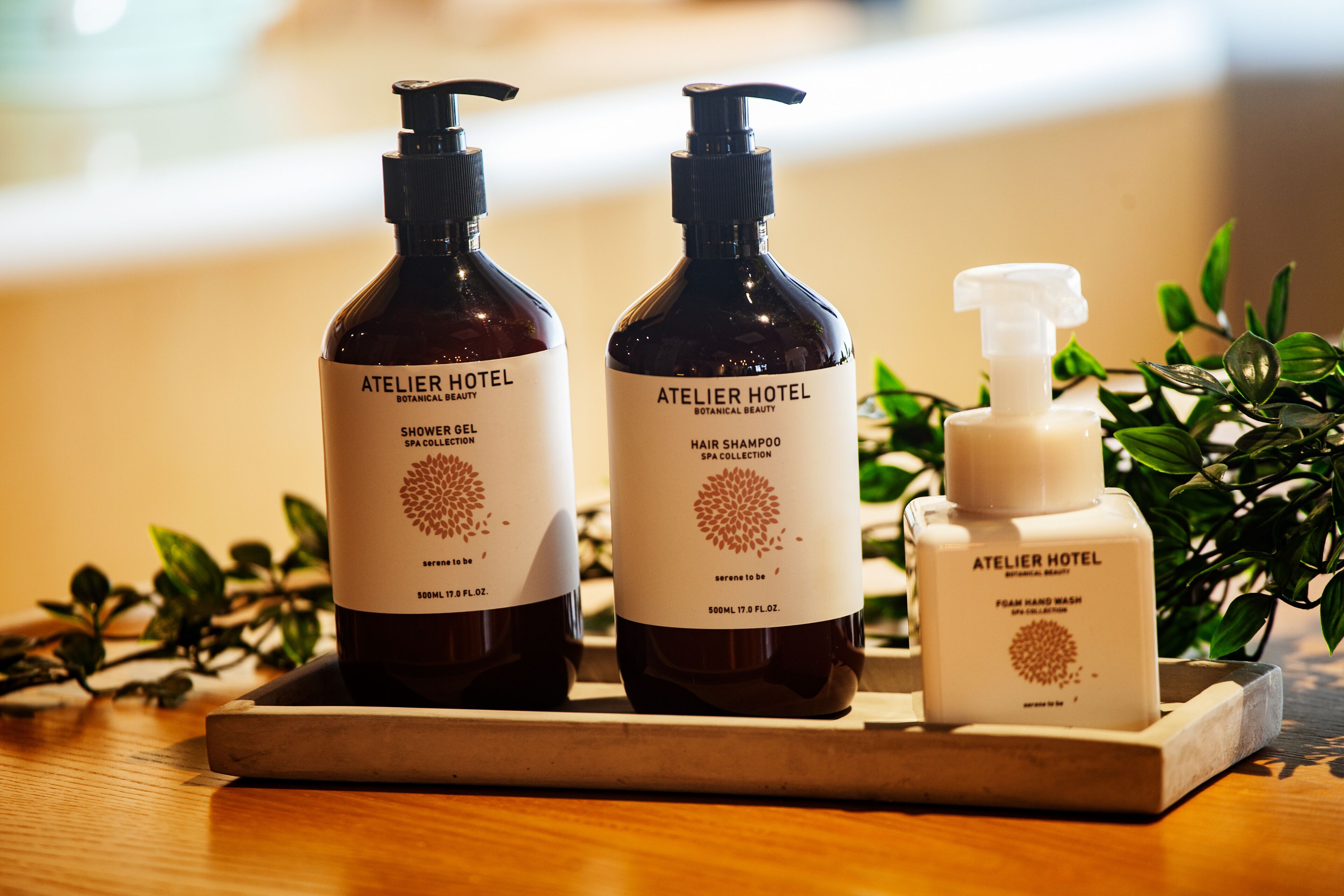 Three bottles of Atelier Hotel spa products on a wooden tray.