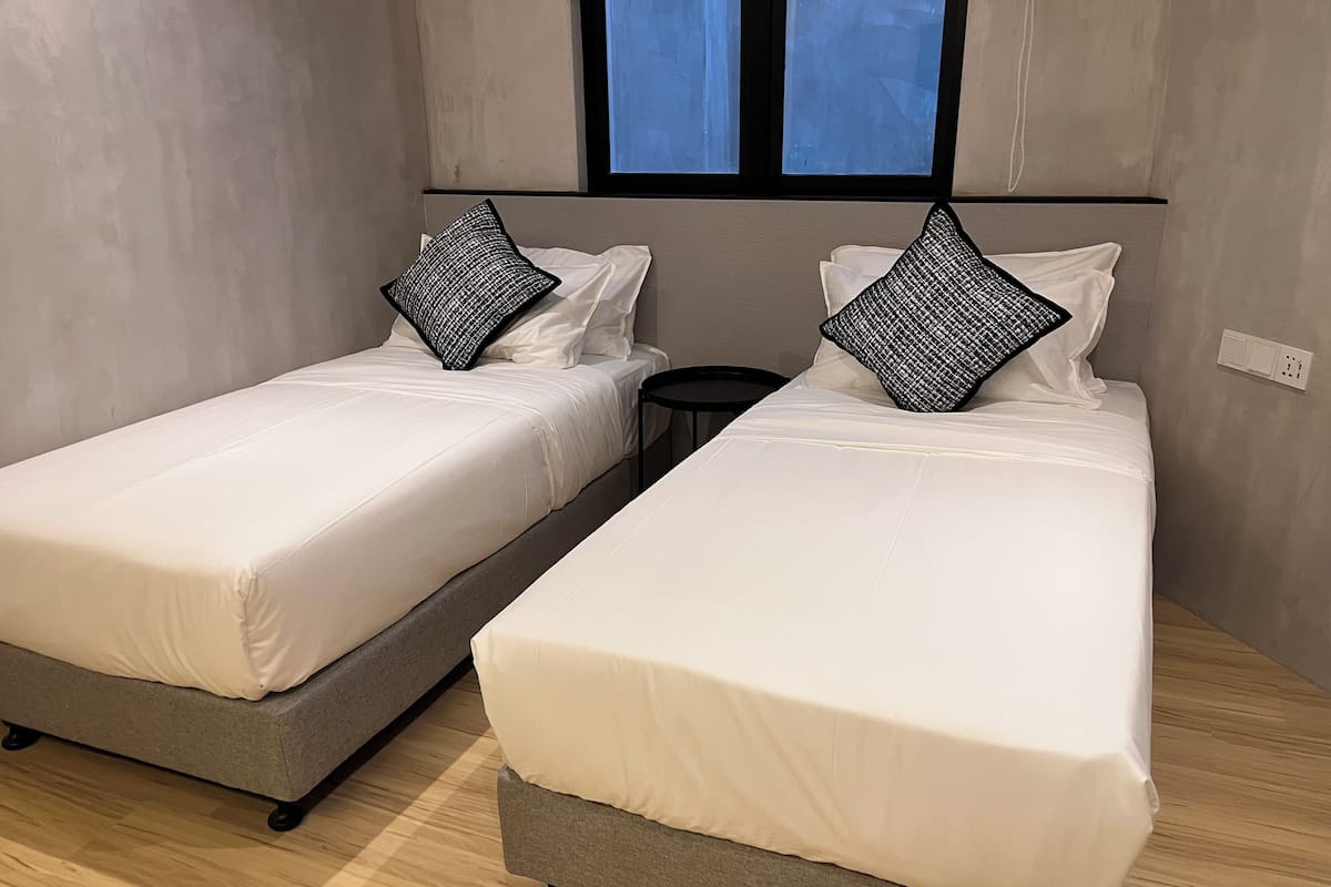 Dos camas individuales con bases grises y ropa de cama blanca, una mesita redonda y una ventana con vistas al cielo.