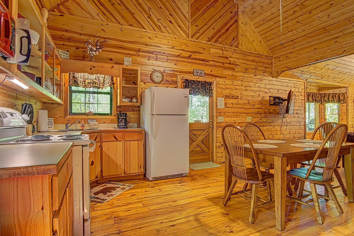 Ein Häuschen-Interieur mit Holzwänden, einer Küche mit Kühlschrank, einem Esstisch mit Stühlen und einem Fenster mit Blick auf Bäume.