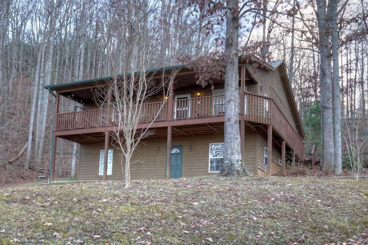 A two-story cabin with a balcony, surrounded by trees.
