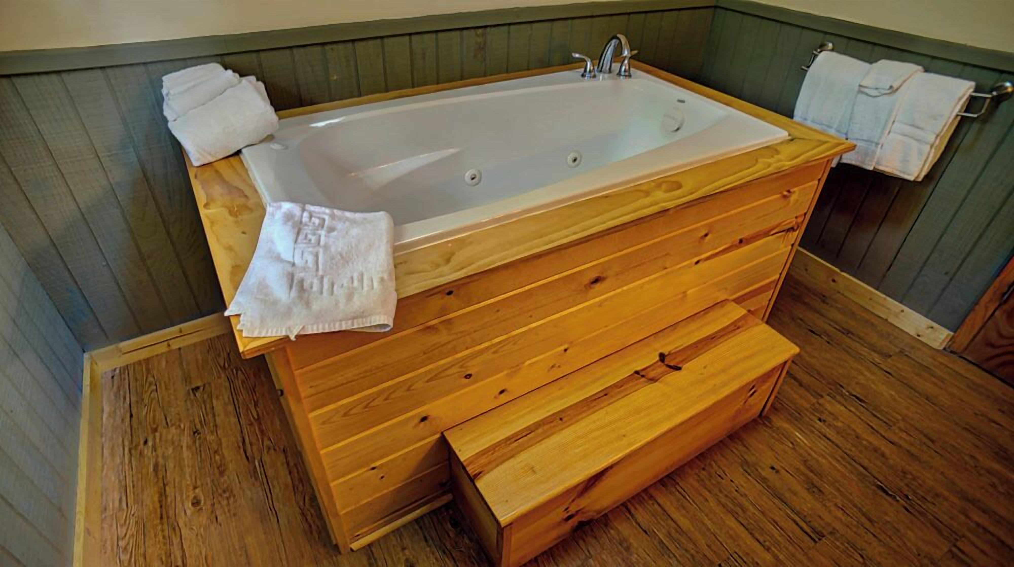 A wooden bathtub with a wooden bench, towels, and a wooden floor.