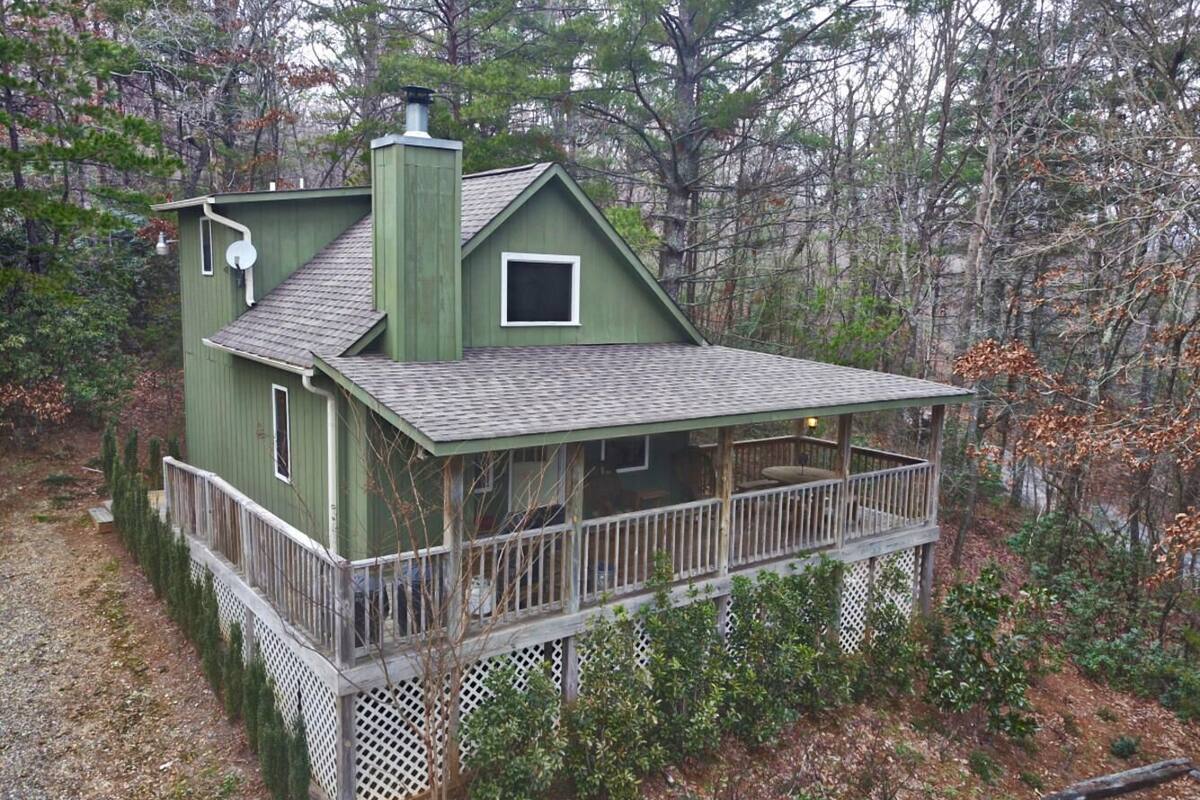 A two-story wooden house with a balcony, surrounded by trees.