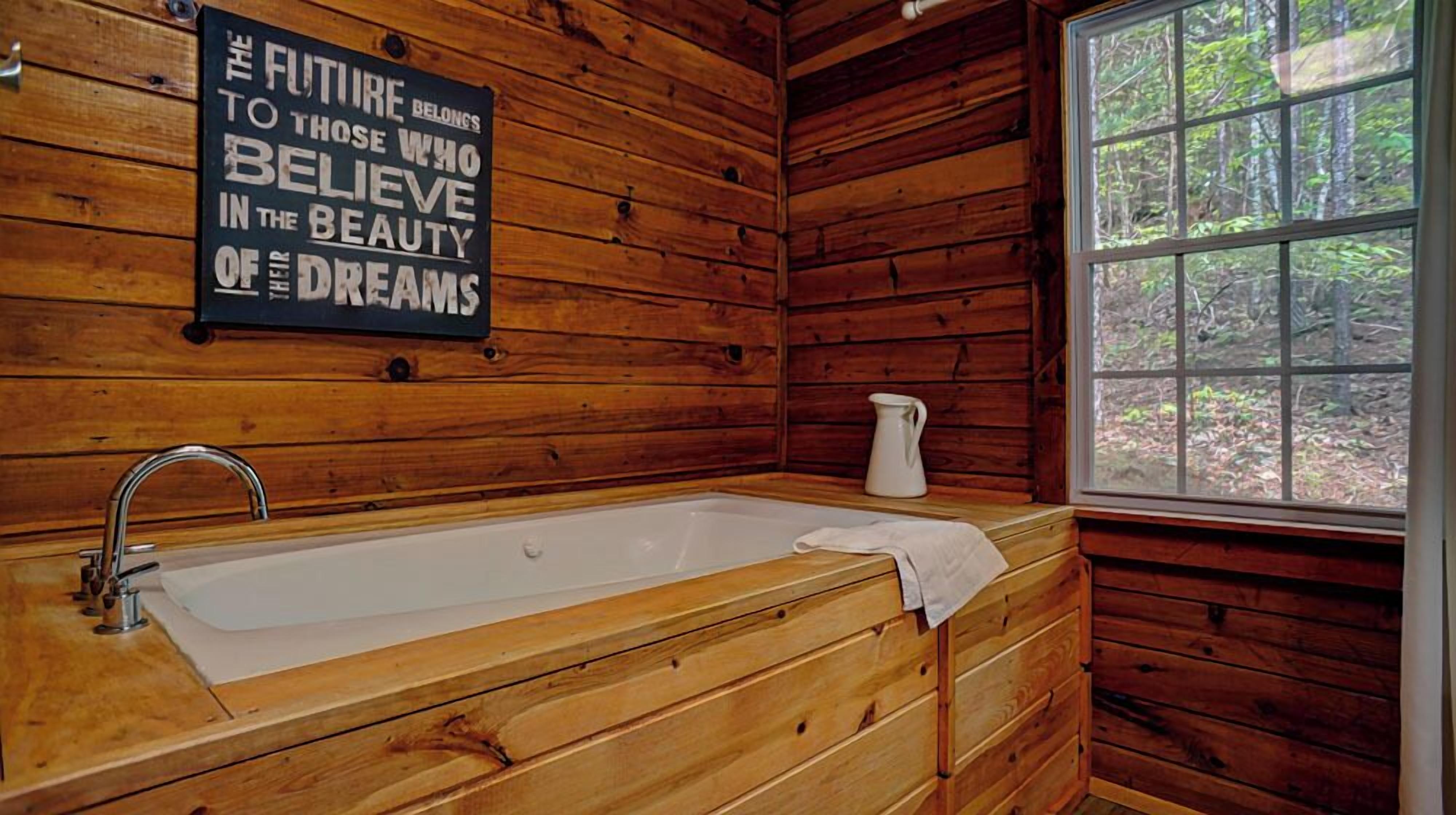 Une salle de bain rustique, aménagée dans une cabane en bois, avec une grande baignoire, un lavabo et une fenêtre donnant sur la forêt.